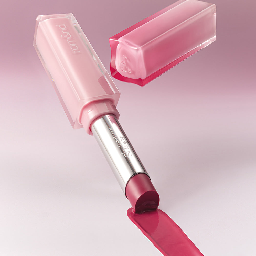 ROMAND Sheer Tinted Stick de la marque ROMAND, stick rose translucide sur fond rose, maquillage en gros plan.