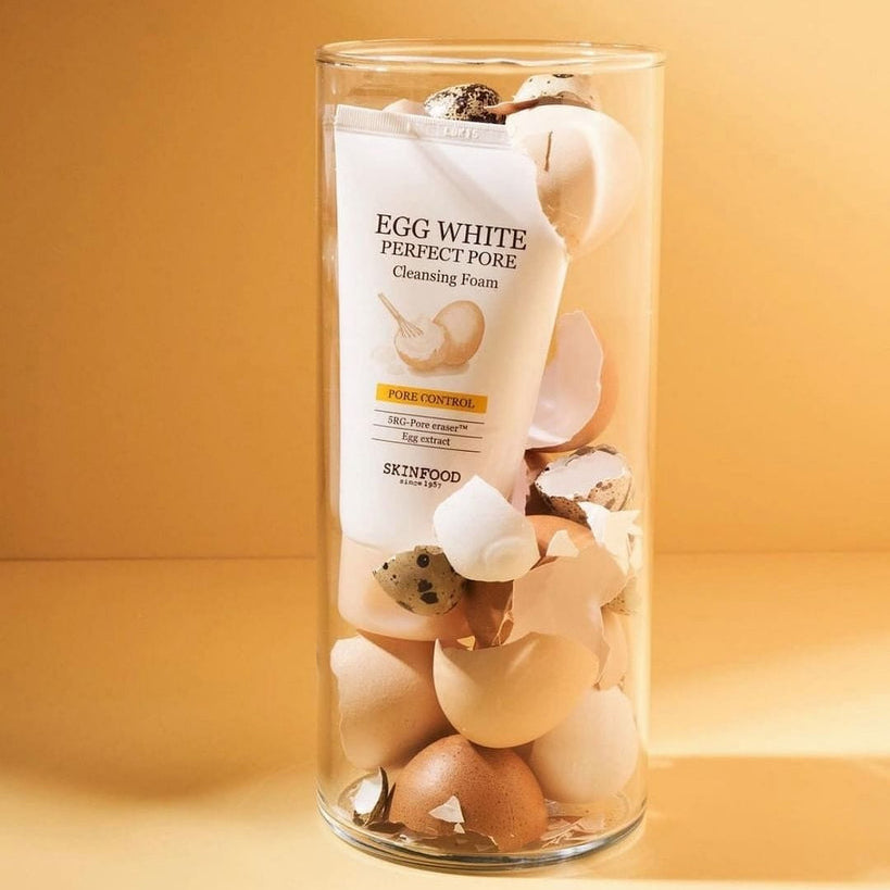 SKINFOOD Egg White Perfect Pore Cleansing Foam 150ml, mousse nettoyante en tube, présentée avec coquilles d’œufs sur fond beige.