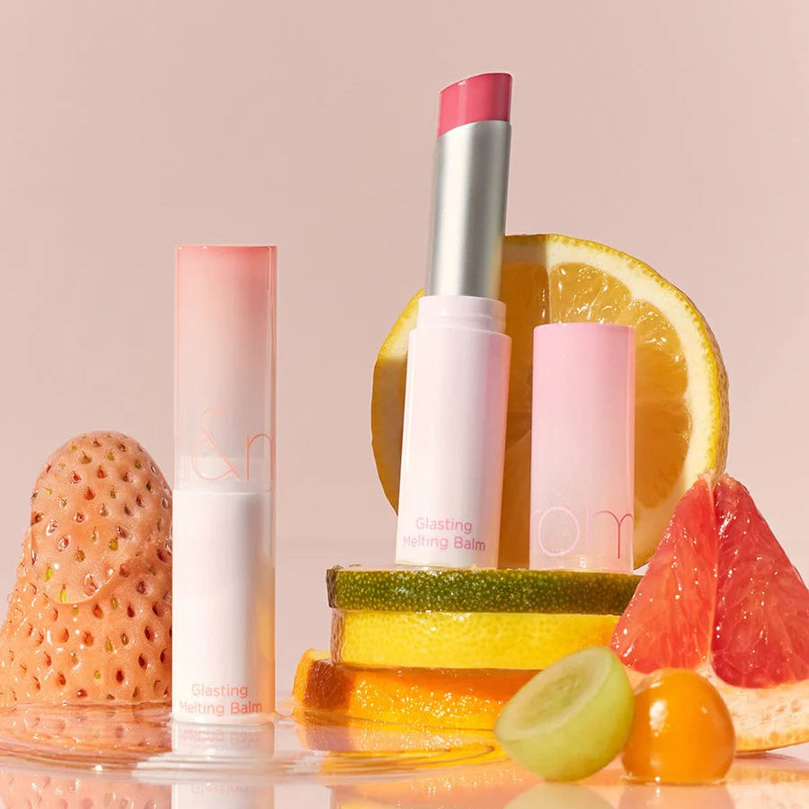 ROMAND Glasting Melting Balm (#01 to #15) de la marque ROMAND, sur fond pastel avec fruits (orange, citron) et baume.