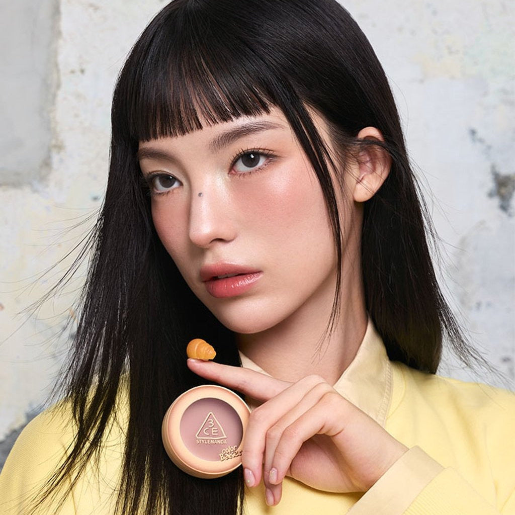 Décris l'image en français : 3CE Color Baker Face Blush, marque 3CE, maquillage sur le visage, jeune femme, pot rose maquillé.