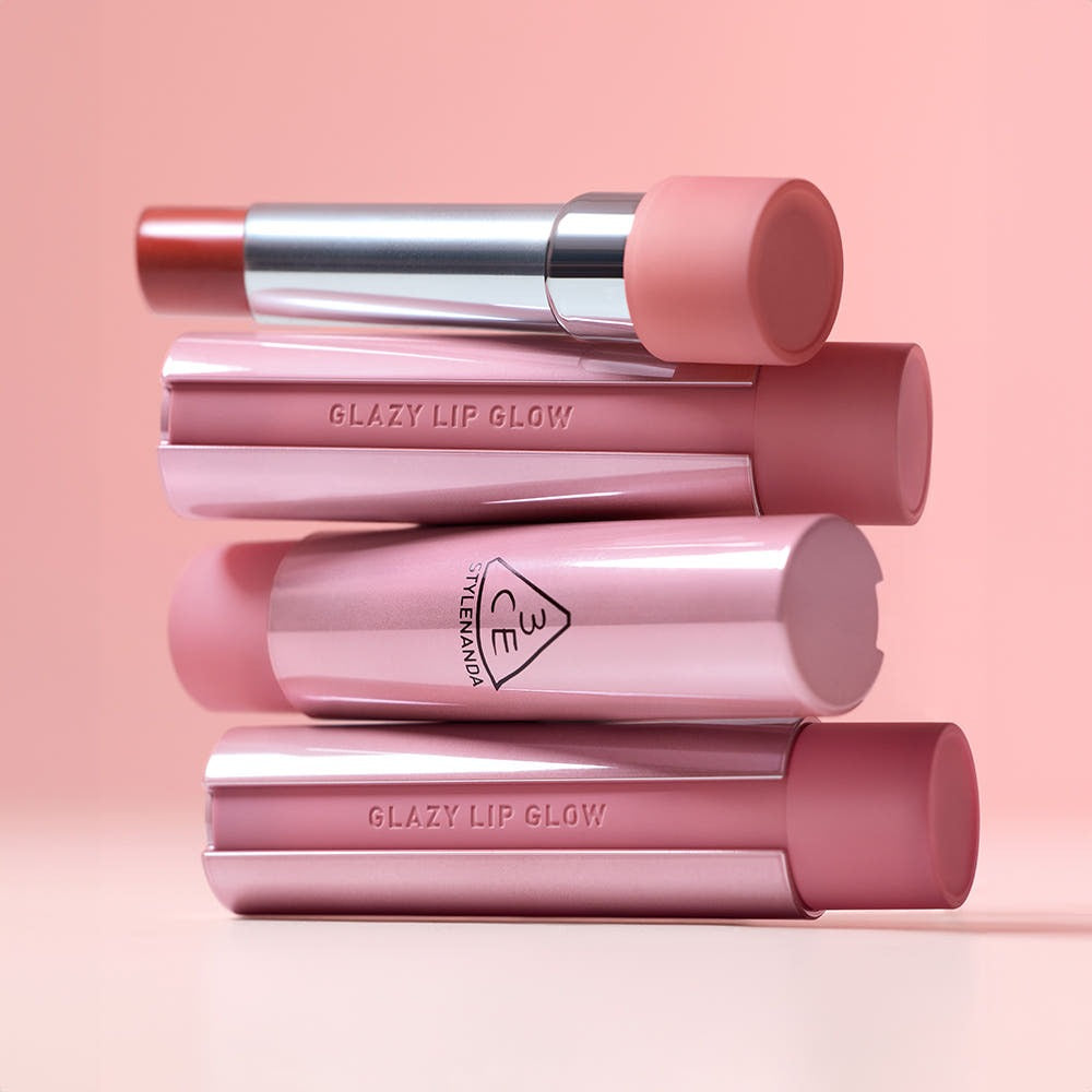 3CE Glaze Lip Glow 3.2g, produit de la marque 3CE : gloss pour lèvres, sur fond rose, tubes empilés, maquillage
