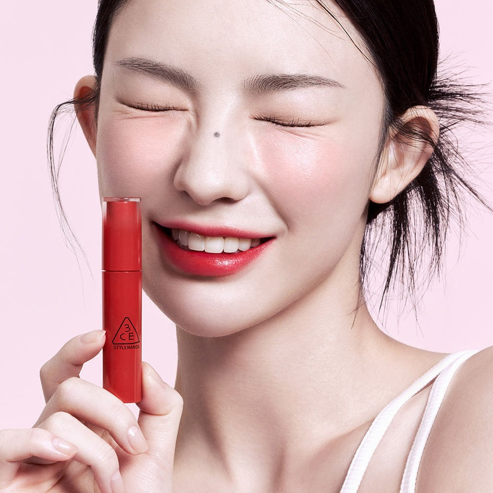 3CE Lazy Pop Lip Stain : la marque 3CE, maquillage sur lèvres rouges et main tenant le lip stain devant fond rose.
