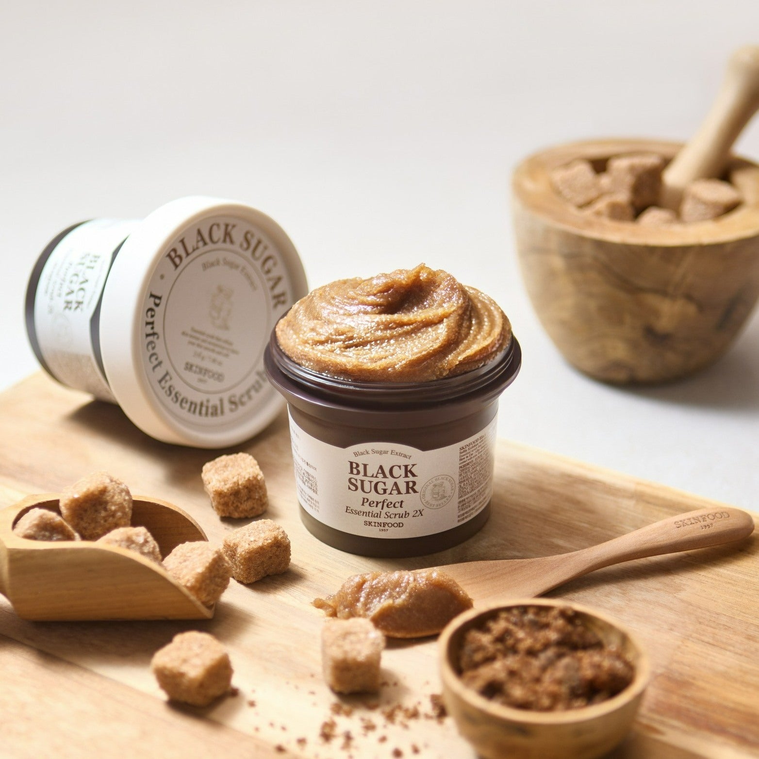 SKINFOOD Black Sugar Perfect Essential Scrub 2x 210g sur table bois, pot et ingrédients de gommage, contexte naturel