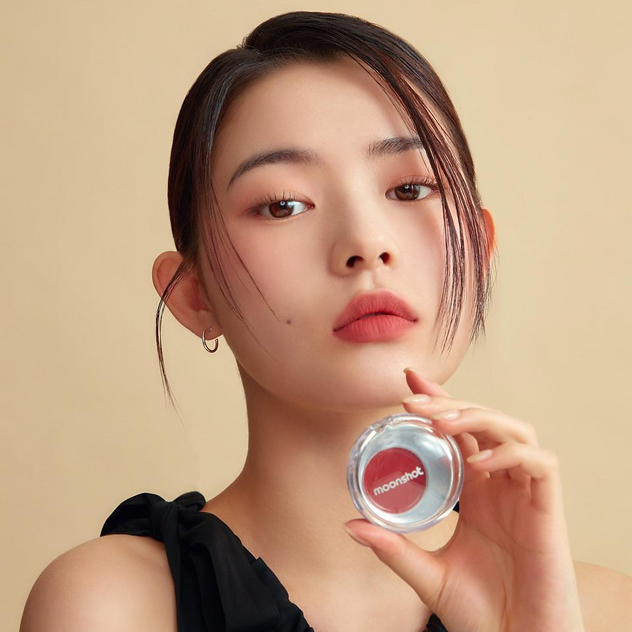 MOONSHOT Melting Mood Lip & Cheek, maquillage sur lèvres et joues, jeune femme tenant le produit, fond beige, photo promo.