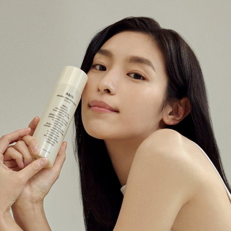 ABIB Jericho Rose PHA Toner Skin Booster 200ml : femme l’application du toner, flacon beige sur fond clair.