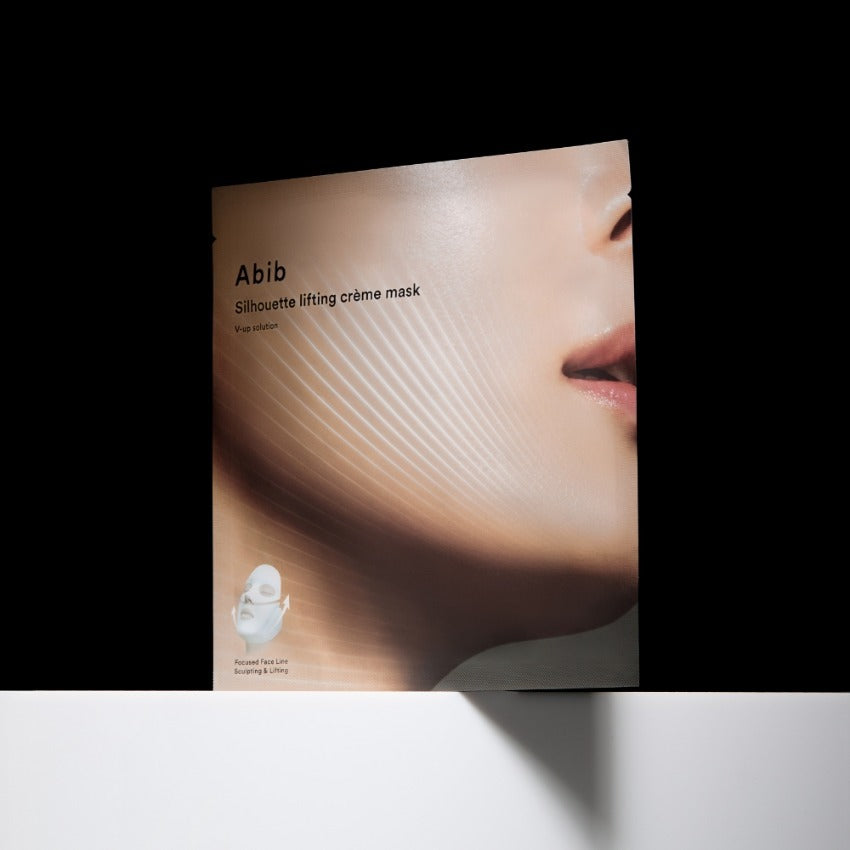 ABIB Silhouette Lifting Cream Mask V-Up Solution, masque liftant Abib sur visage, packaging sur fond noir, lumière douce.