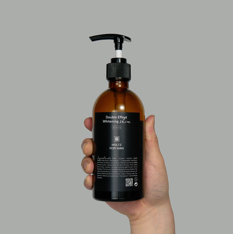Main tenant ANNA HOLTZ For Men Double Effect Whitening Skin Toner 300ml, flacon ambré pompe, fond gris, produit marque