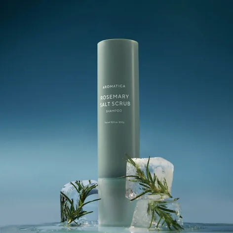 AROMATICA Rosemary Salt Scrub Shampoo, flacon vert sur fond bleu, feuilles et cristaux de sel, contexte spa.