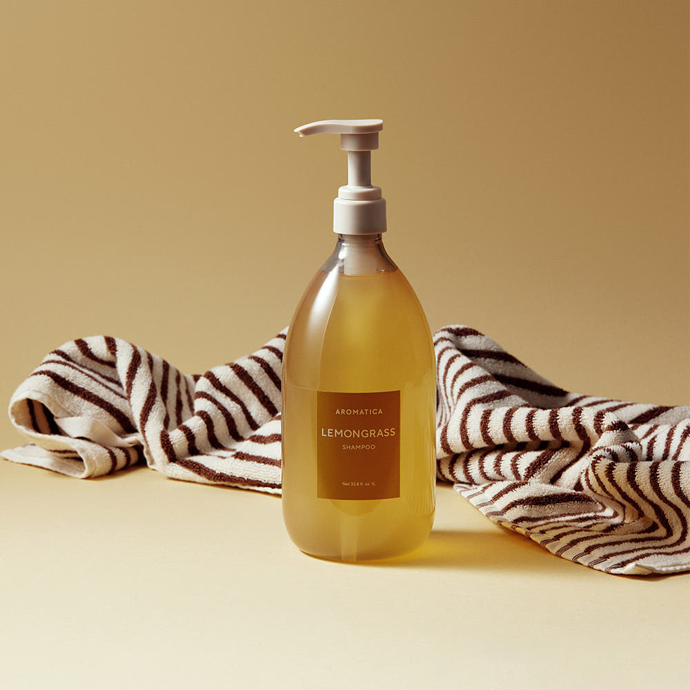 AROMATICA Life Lemongrass Shampoo 1000ml de la marque AROMATICA, posé sur serviettes rayées, fond beige clair.
