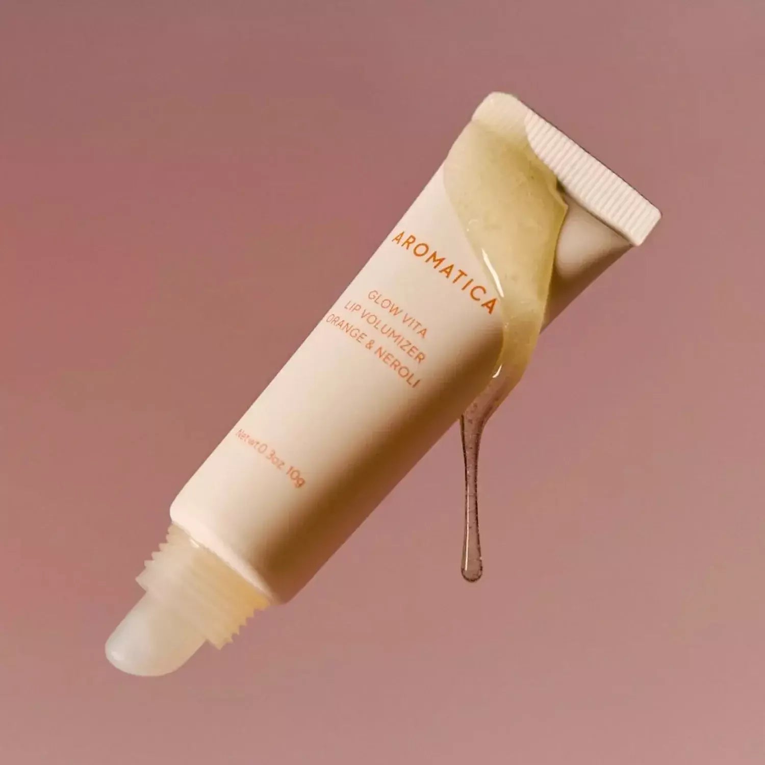 AROMATICA Glow Vita Lip Volumizer Orange & Neroli de la marque AROMATICA, tube sur fond rose, goutte de gloss