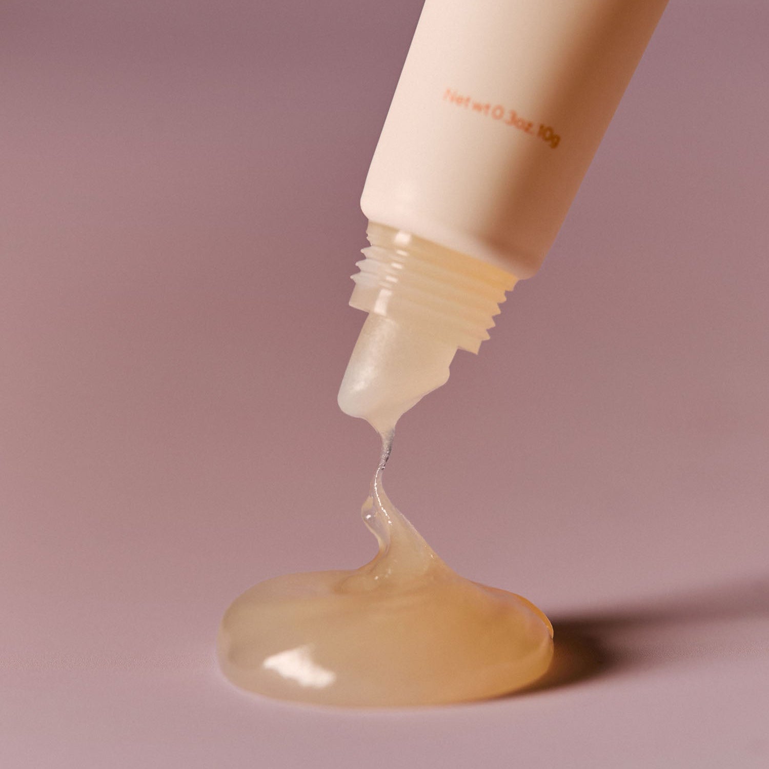 AROMATICA Glow Vita Lip Volumizer Orange & Neroli, tube appliquant un gel lumineux sur lèvres, fond rose studio.