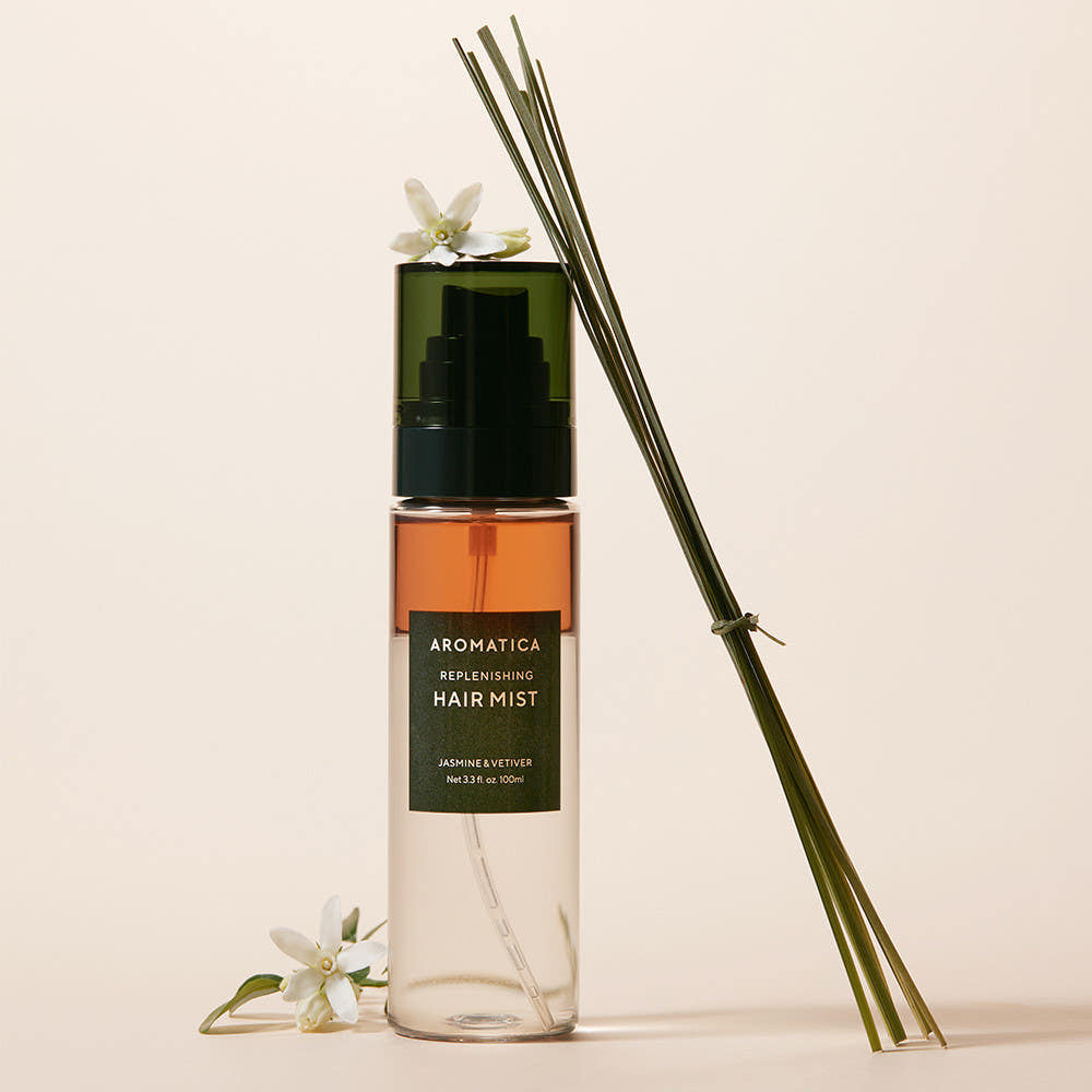 AROMATICA Replenishing Hair Mist Jasmine & Vetiver 100ml, flacon sur fond beige avec fleurs blanches et diffuseur d’ambiance.