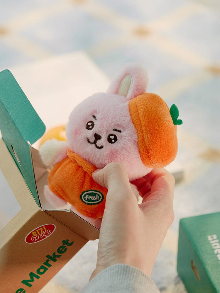 BT21 COOKY BABY PLUSH ORANGE PARTY : peluche orange de COOKY dans un carton Market fraîchement ouvert, décor chambre.
