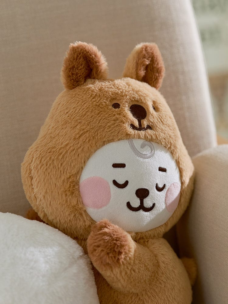 BT21 RJ BABY LYING DOLL FLUFFY : peluche officielle LINE FRIENDS, bébé alpaga RJ allongé sur canapé, décor cocooning.