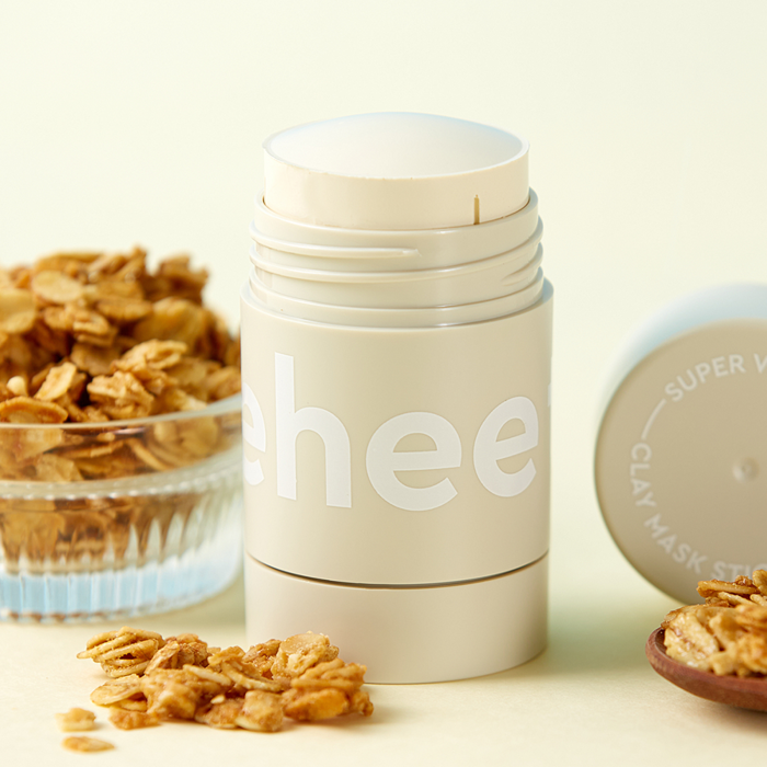 Décris l'image en français : CHARMZONE Teeheehee Soothing Oat Clay Mask Stick 35g, stick à l’avoine, décor fleurs d’avoine.