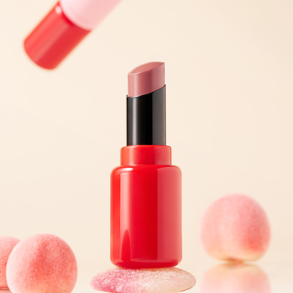 COSIERO Jealousy Plumper de COSIERO, rouge à lèvres sur fond beige avec accessoires maquillage en ambiance douce