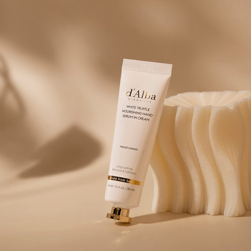 Décris l'image en français : D'ALBA Nourishing Hand Serum In Cream 30ml, tube crème sur fond beige avec mains/texture.