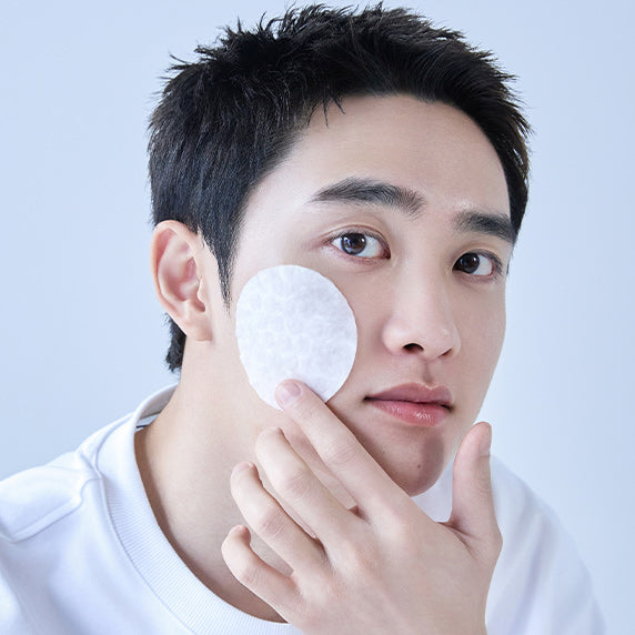 Décris l'image en français : DERMATORY Hyaluronic Acid Moisture Spring Embo Pad Refill 60 sheets, homme appliquant un pad rond.