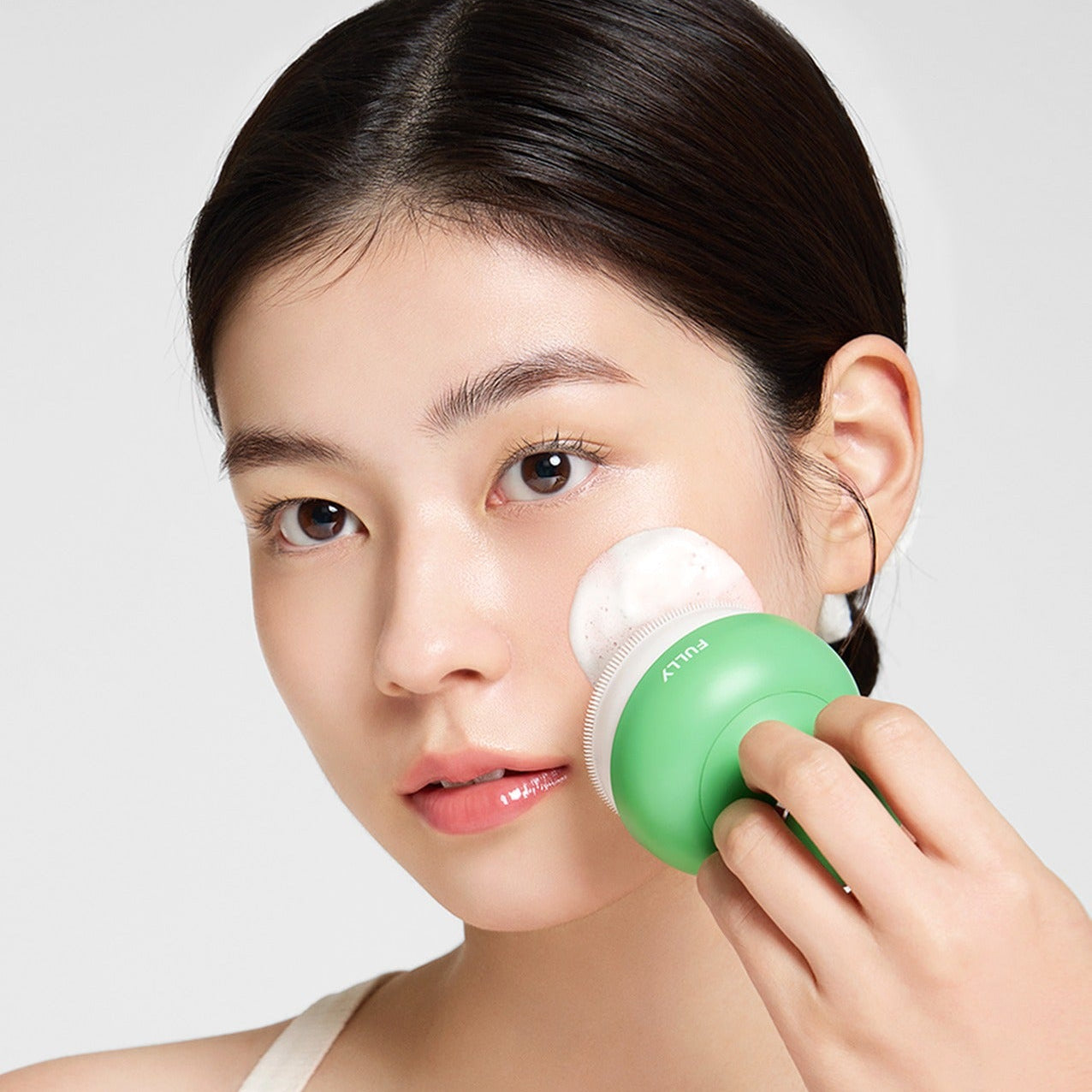 FULLY Pore brush, visage en gros plan utilisant la brosse pour nettoyer les pores, marque FULLY, fond clair.