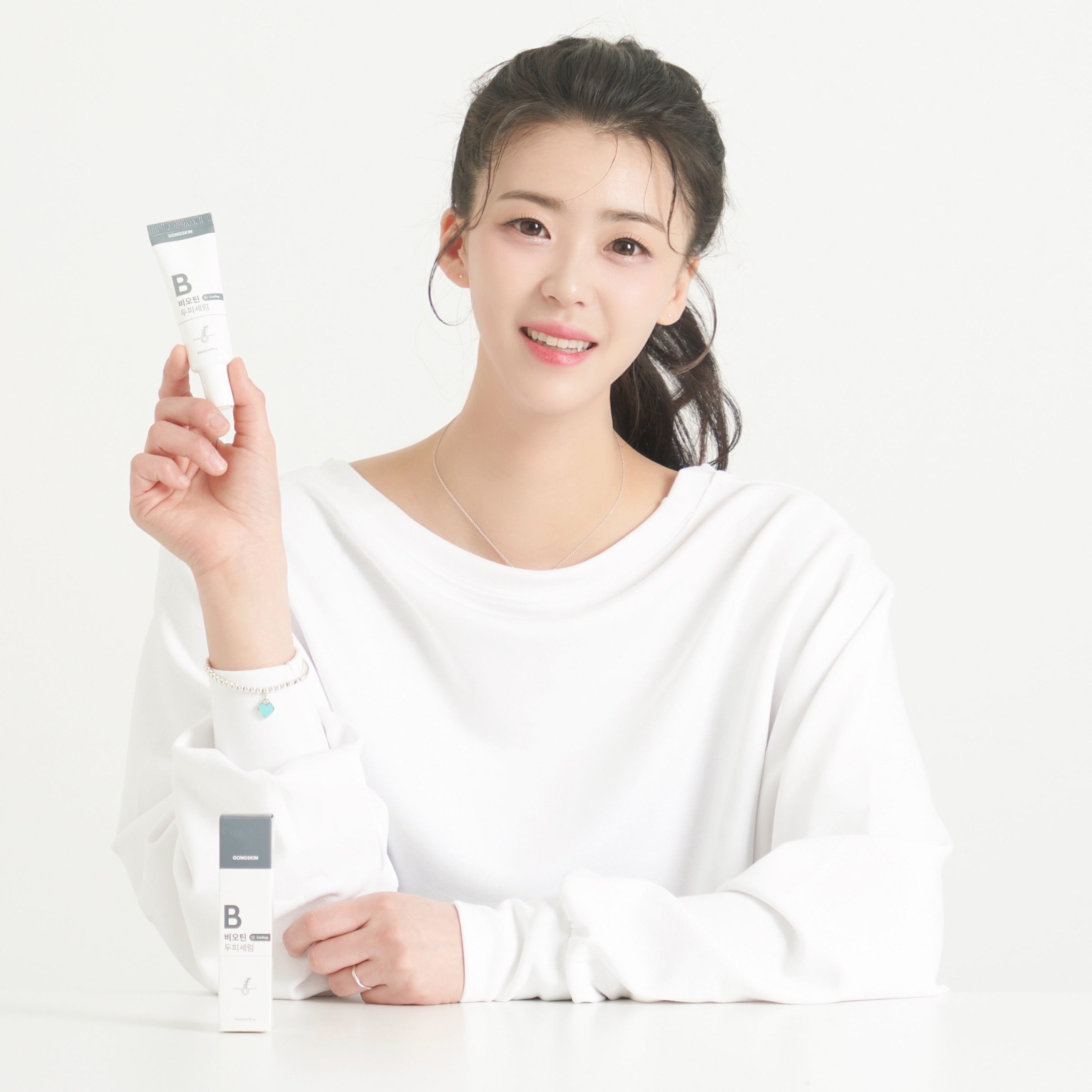 Décris l'image en français : GONGSKIN Biotin Cooling Scalp Serum 20ml, marque montrée par une femme tenant le flacon sur fond clair.