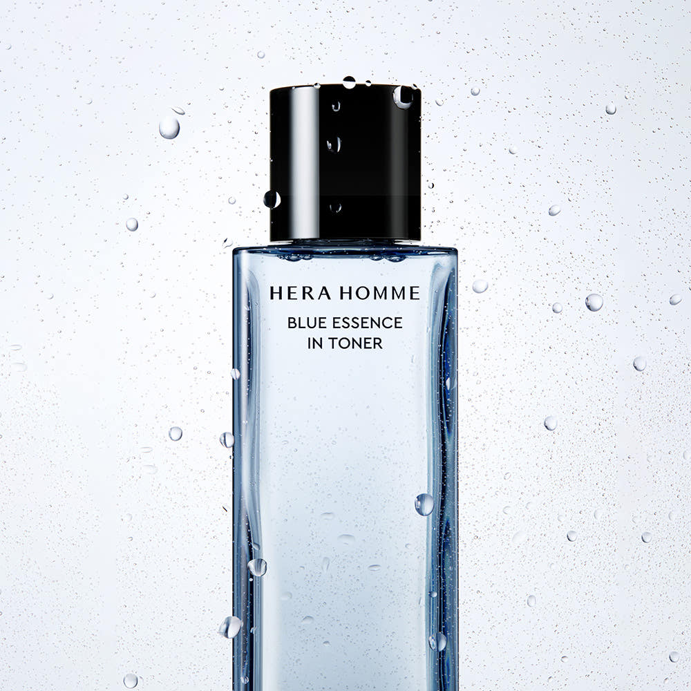 HERA Homme Blue Essence In Toner 125ml : flacon noir/bleu sur fond clair avec gouttes d’eau, design salle de bain.