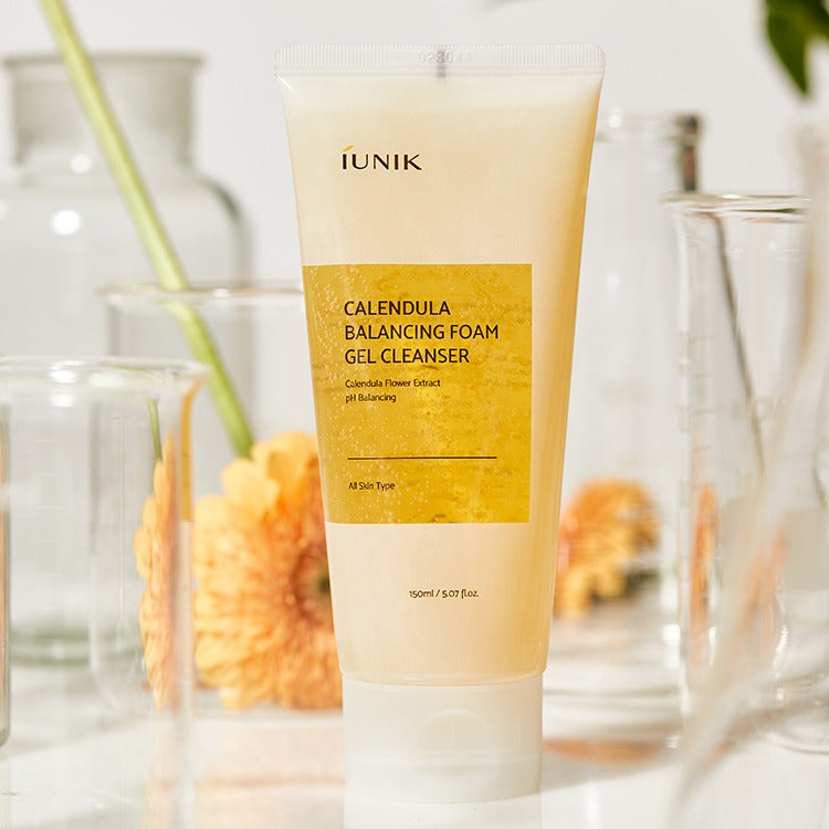 IUNIK Calendula Balancing Foam Gel Cleanser 150ml, tube IUNIK sur fond salle de bain, fleurs de souci en arrière-plan.