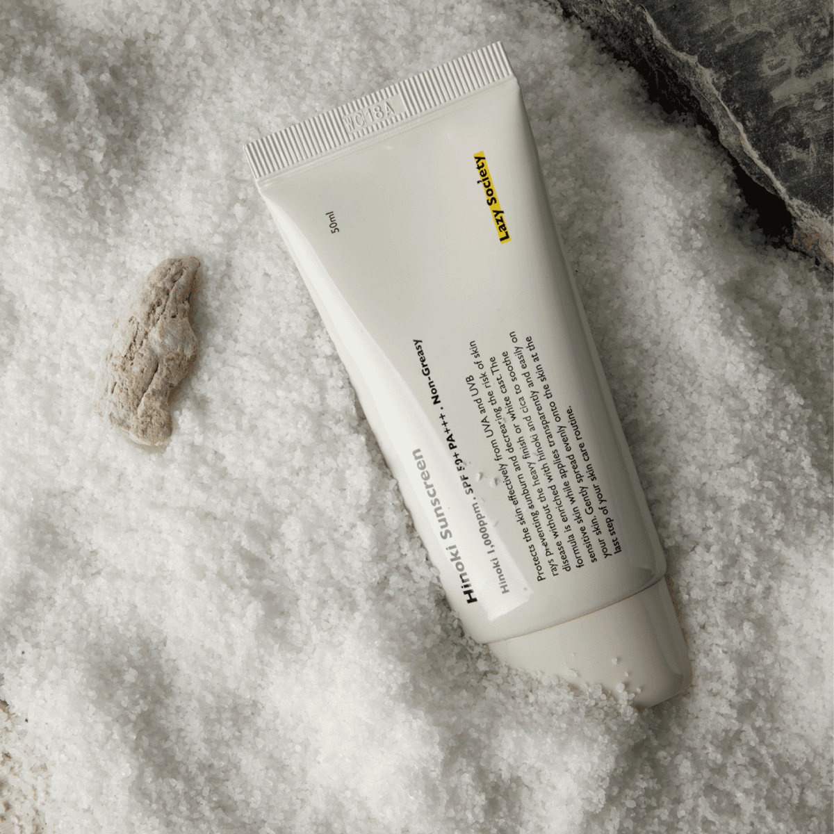 Décris l'image en français : LAZY SOCIETY Hinoki Sunscreen SPPF 50+ PA+++ 50ml, tube crème sur fond texturé, marque au visuel.