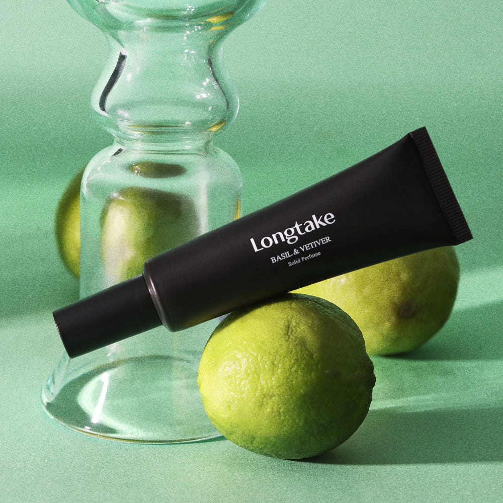 LONGTAKE Solid Perfume 30ml de LONGTAKE : tube noir et agrume sur fond vert, contexte visuel studio.