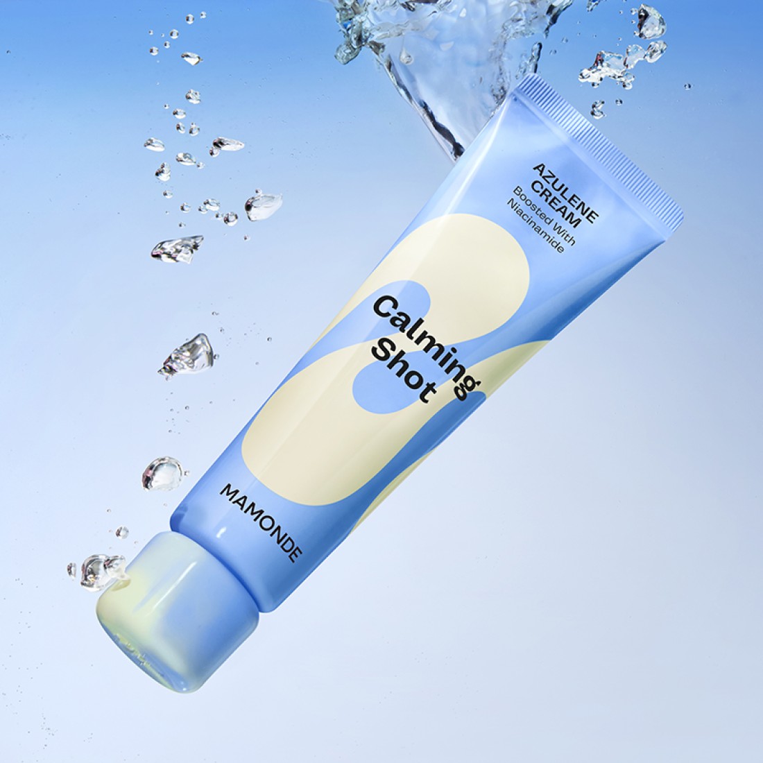 Décris l'image en français : MAMONDE Calming Shot Azulene Cream 60ml, tube bleu, éclaboussures d’eau sur fond bleu clair.