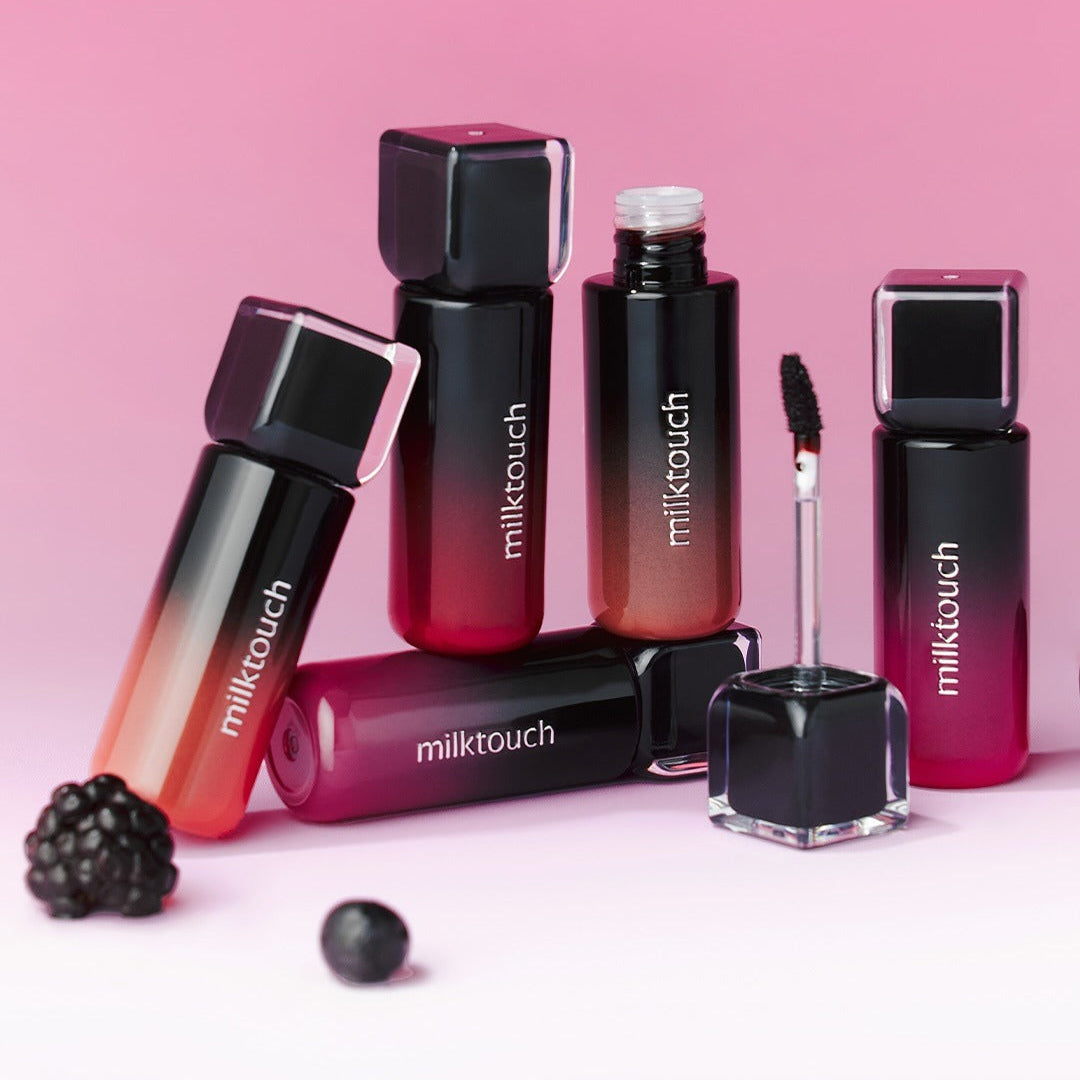 Décris l'image en français : MILK TOUCH Black Peel-Off Lip Tattoo, flacons et applicateur maquillage sur fond rose.