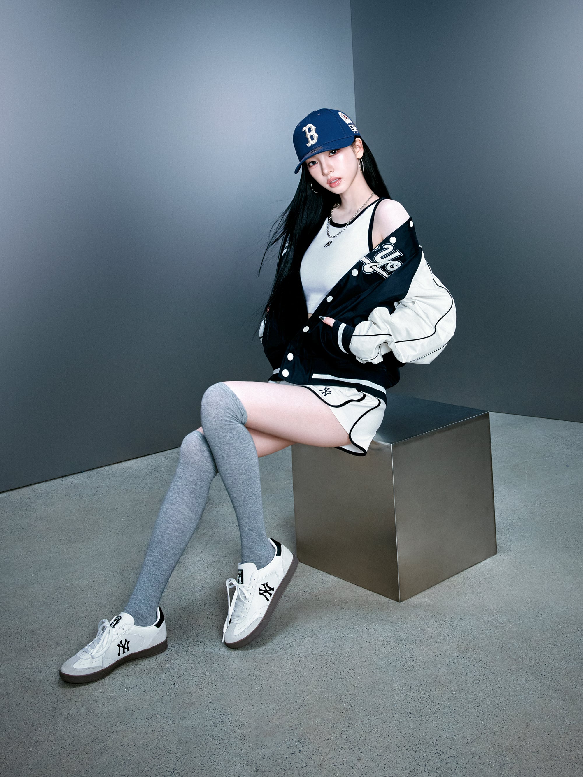 Décris l'image en français: MLB Clubby New York Yankees WHITE, modèle stylé sur fond studio, chapeau et tenue blanche/bleue.