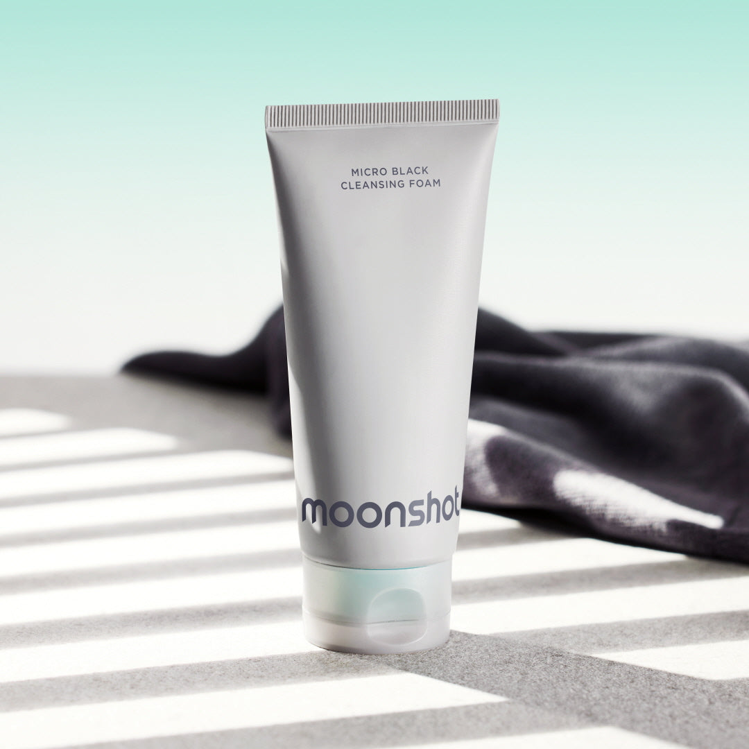 MOONSHOT Micro Black Cleansing Foam, tube noir et blanc sur drap noir et fond clair, photo produit au soleil.