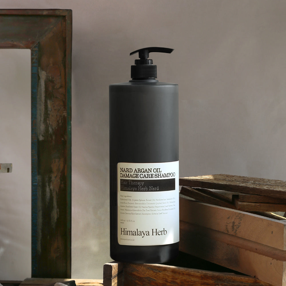 Décris l'image en français : NARD Argan Oil Damage Care Shampoo 1500ml de NARD, flacon noir sur bois, lumière naturelle.