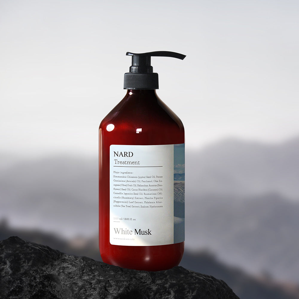 NARD Repairing Perfumed Treatment 1000ml de NARD, flacon noir pompe sur roche, parfum White Musk, fond montagnes flou.