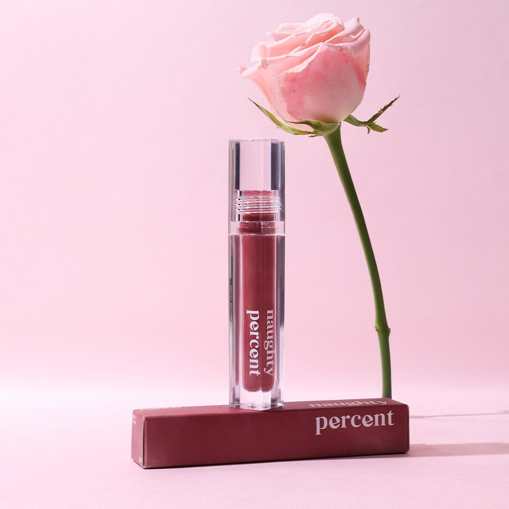 NAUGHTY PERCENT Matte Bloom Tint de la marque NAUGHTY PERCENT, flacon sur fond rose avec une rose en contexte beauté.