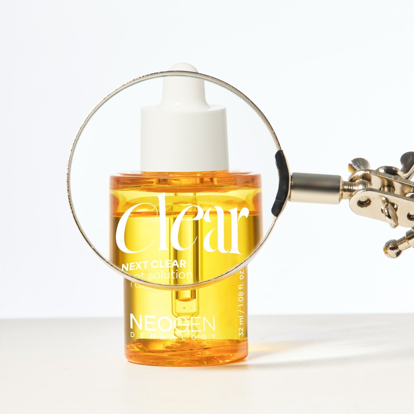NEOGEN Next Clear Spot Solution 32ml, flacon jaune avec loupe sur fond clair : soin anti-imperfections.