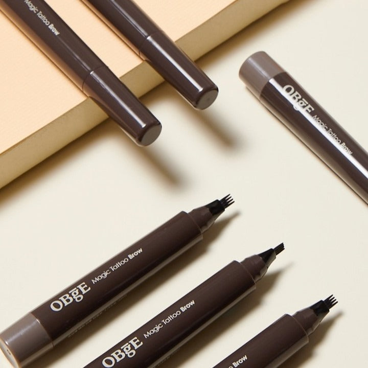 OBGE Magic Tattoo Brow de la marque OBGE : crayons sourcils bruns sur fond beige, vue rapprochée maquillage.