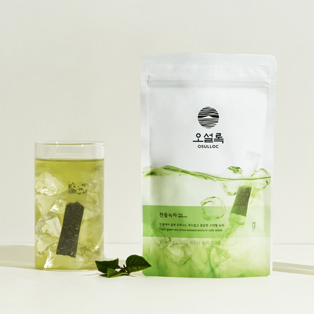 OSULLOC Cold Green Tea 20p : sachet et thé vert glacé dans un verre, feuilles de thé sur fond clair.