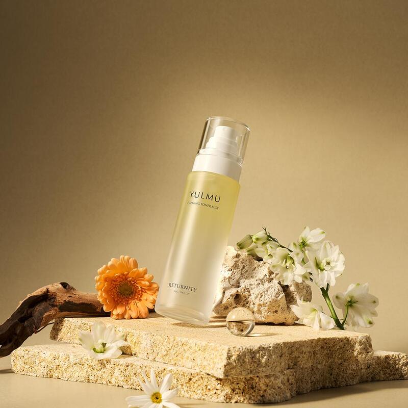 RETURNITY Yulmu Calming Toner Mist 100ml, brume apaisante de la marque RETURNITY, sur socle beige avec fleurs, fond studio.