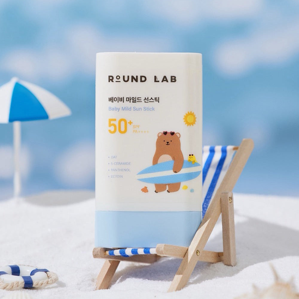 ROUND LAB Baby Mild Sun Stick SPF 50+ PA++++ 21g sur une plage avec un ours décoratif, protection solaire douce pour bébé.
