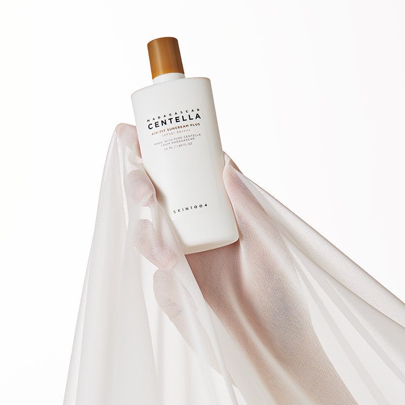SKIN1004 Madagascar Centella Air-fit Sunscreen Plus 50ml en main avec un voile blanc subtil en arrière-plan, accentuant son élégance.