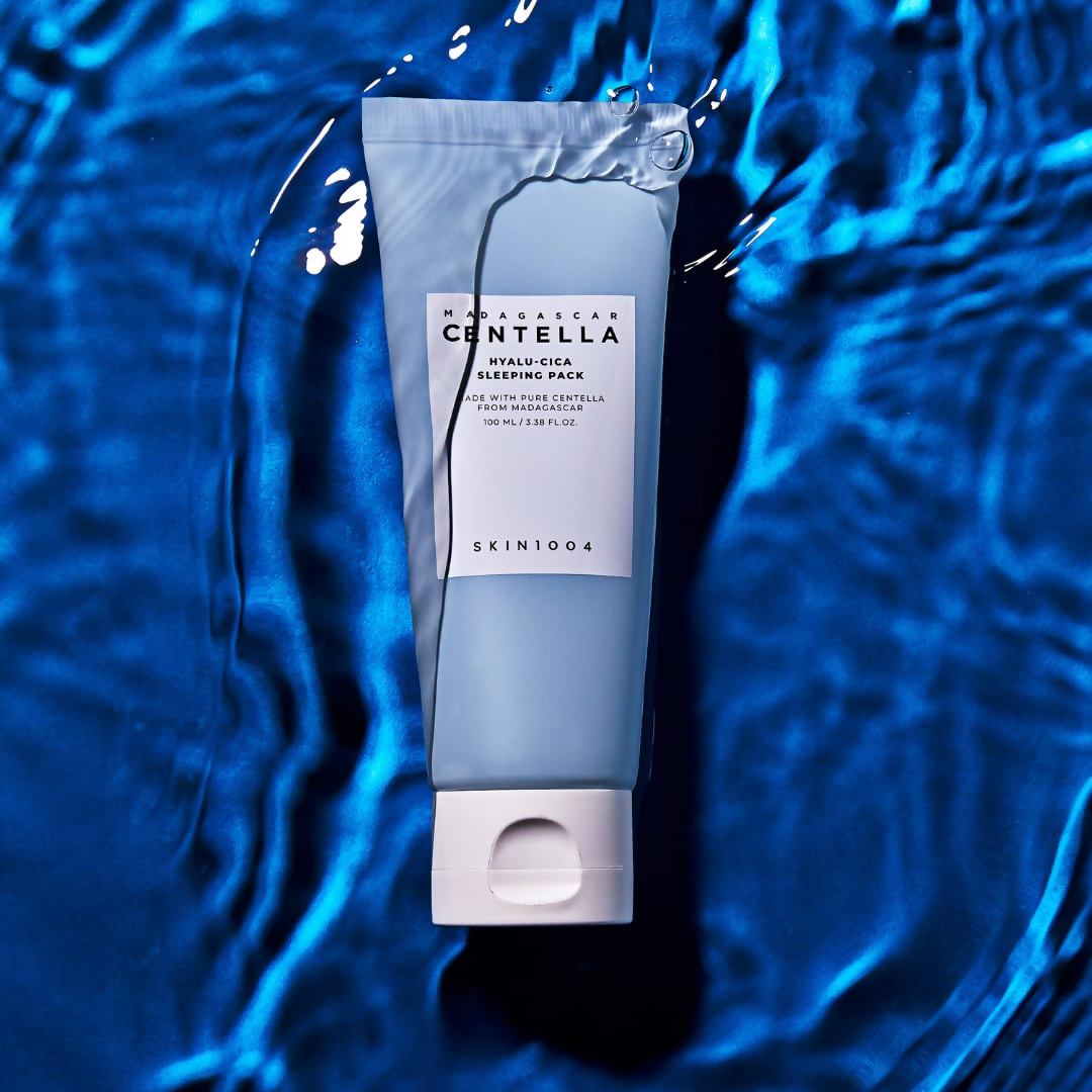 La crème hydratante SKIN1004 Madagascar Centella Hyalu-Cica Acid Sleeping Pack 100ml posée sur un arrière-plan bleu aquatique.