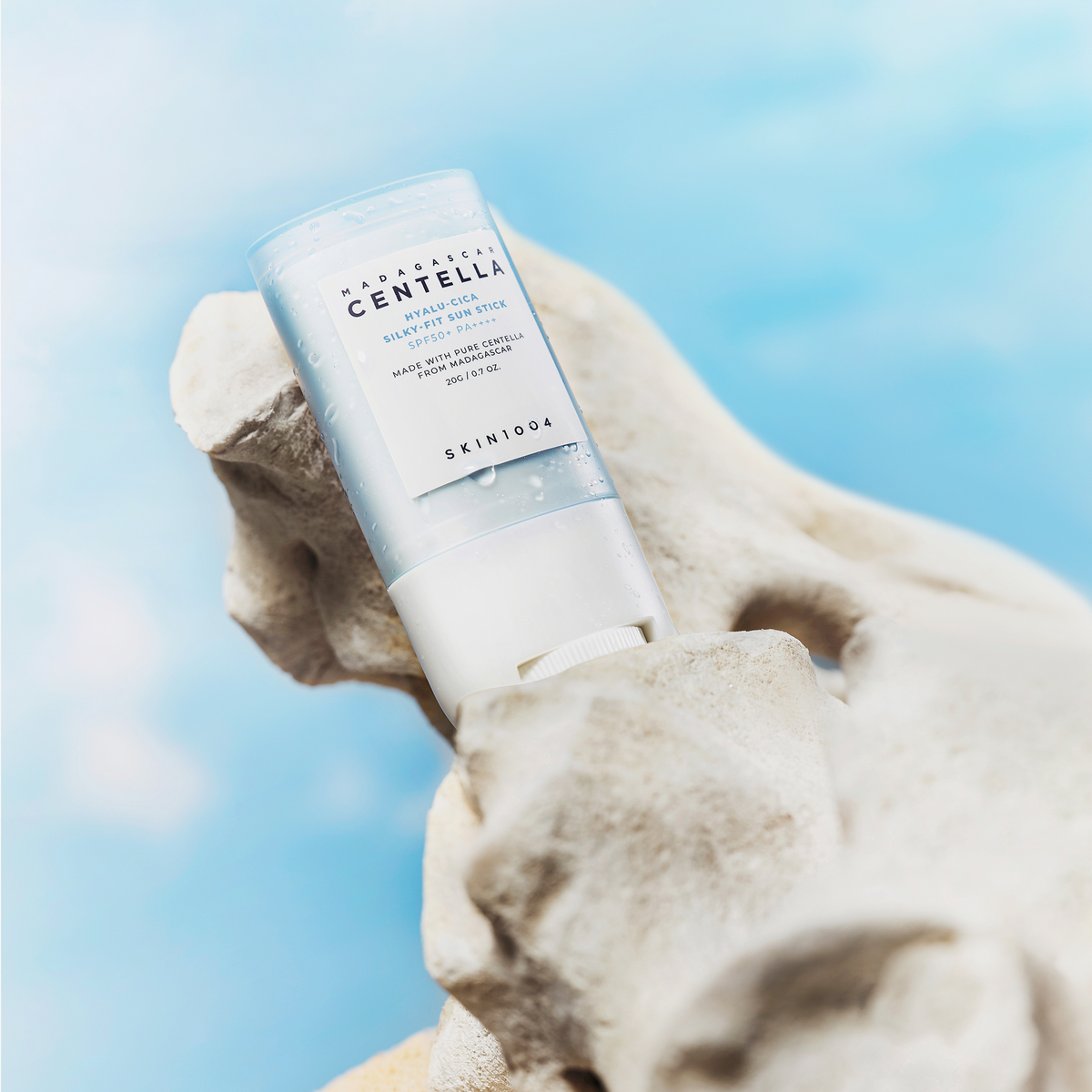 SKIN1004 Madagascar Centella Hyalu-Cica Silky Fit Sun Stick 20g posé sur une roche avec ciel bleu en arrière-plan