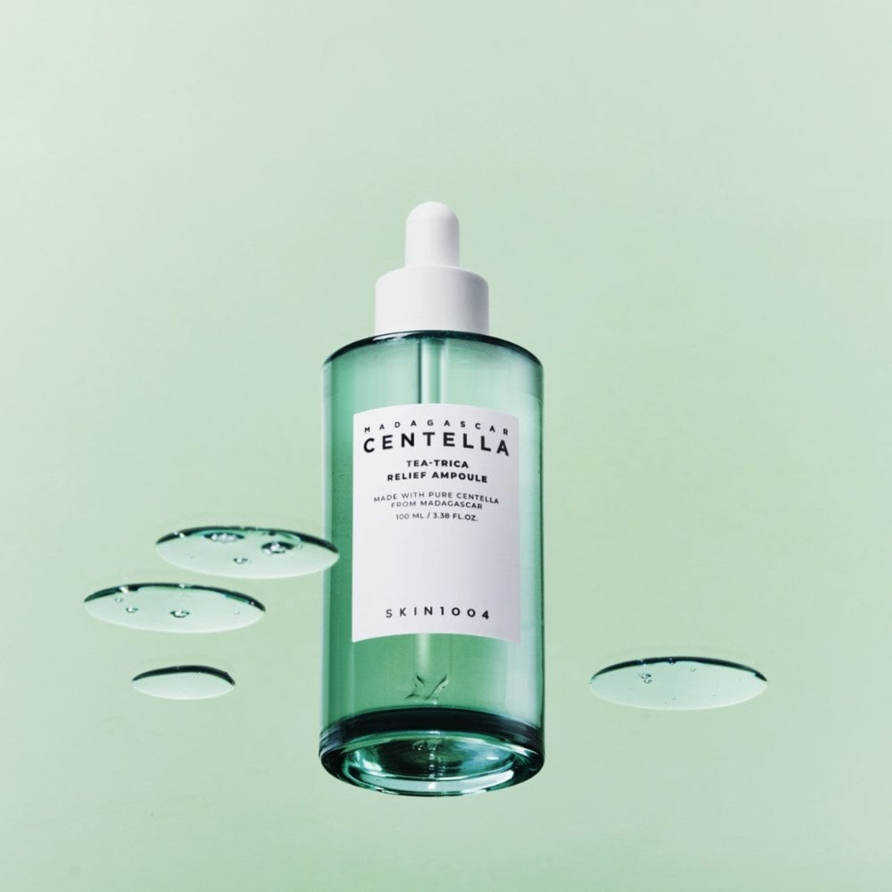 SKIN1004 Madagascar Centella Tea-trica Relief Ampoule 100ml, sérum apaisant hydratant au centella, fond vert avec gouttelettes.