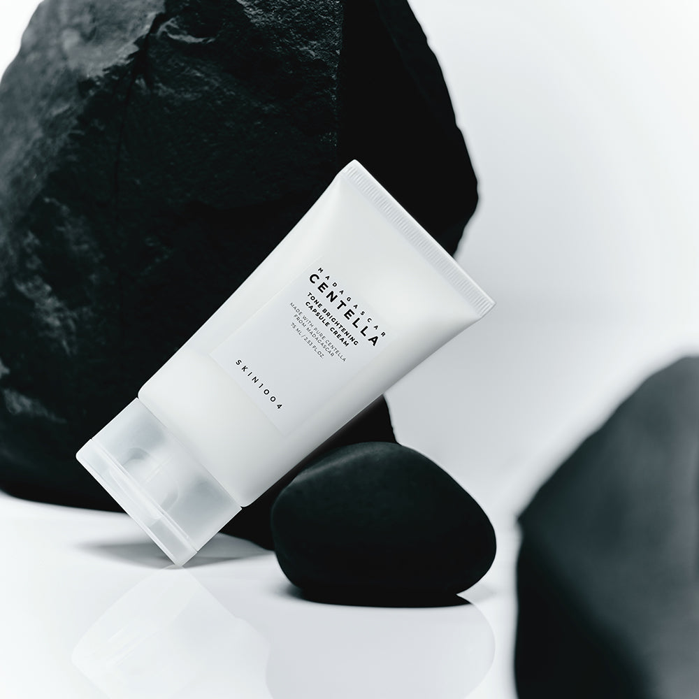 Crème SKIN1004 Madagascar Centella Tone Brightening Capsule 75ml posée sur des roches noires, fond minimaliste moderne.