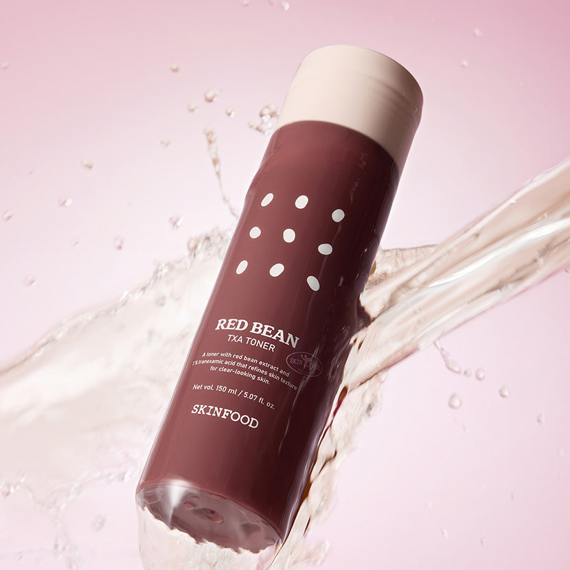 SKINFOOD Red Bean Tranexamic Acid Toner 150ml, bouteille sur fond rose avec éclaboussures d’eau, visuel produit.