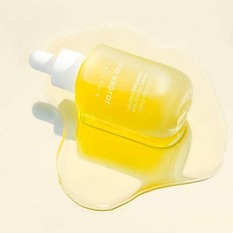 S.NATURE Jojoba Oil 30ml de la marque S.NATURE, flacon jaune sur fond clair, goutte d'huile en contexte beauté