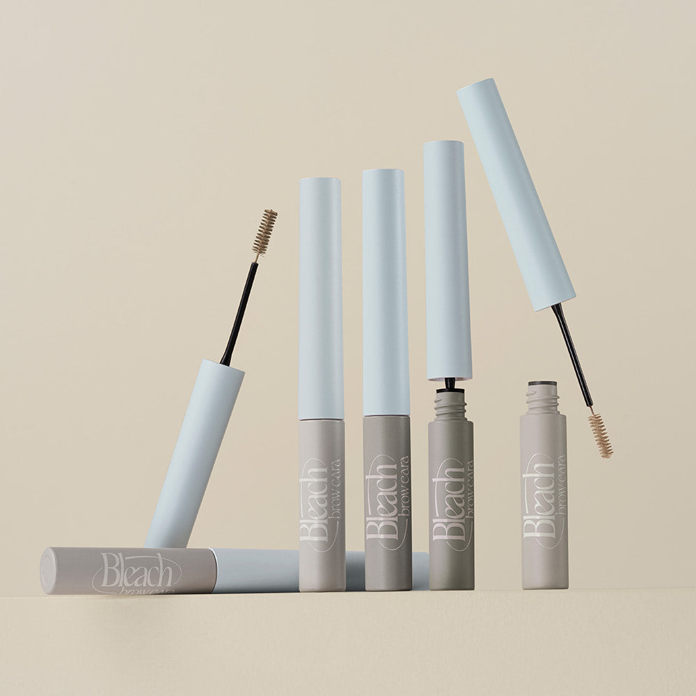 Décris l'image en français: TOO COOL FOR SCHOOL Bleach Brow Cara, tubes et brosses brow, produits sur fond clair.