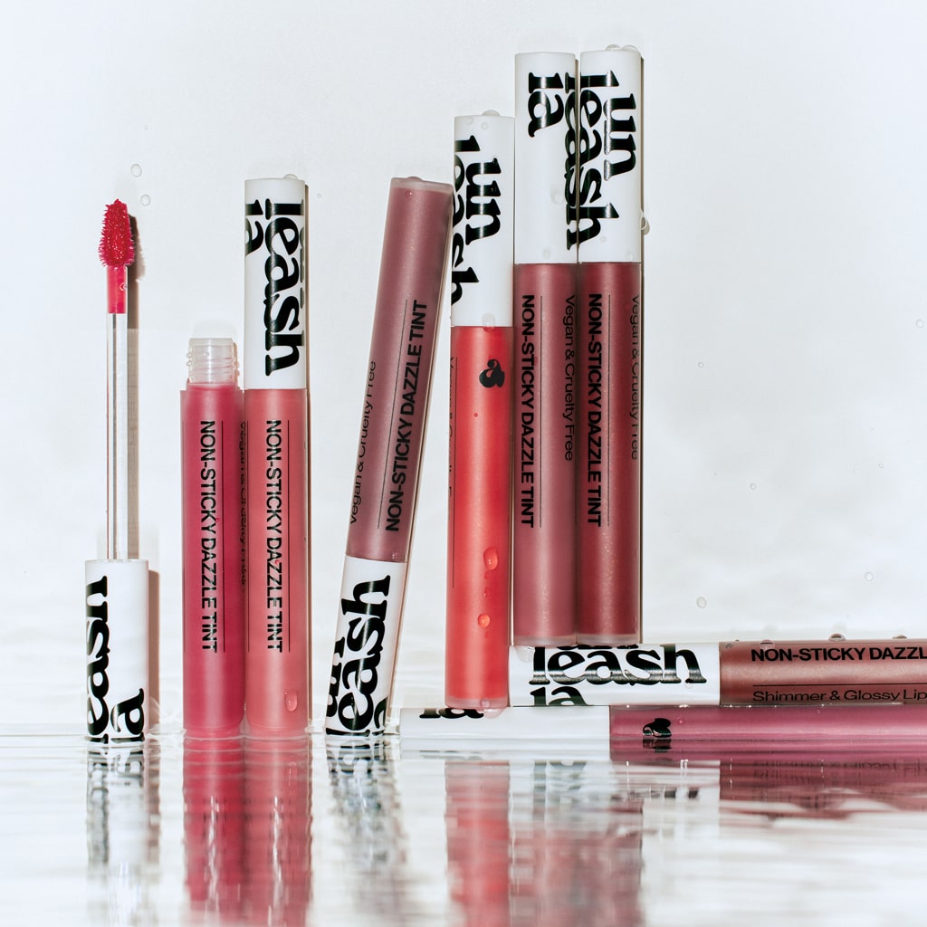 UNLEASHIA Non-Sticky Dazzle Tint, gloss non collant de la marque, sur fond blanc, tubes et applicateurs maquillage.