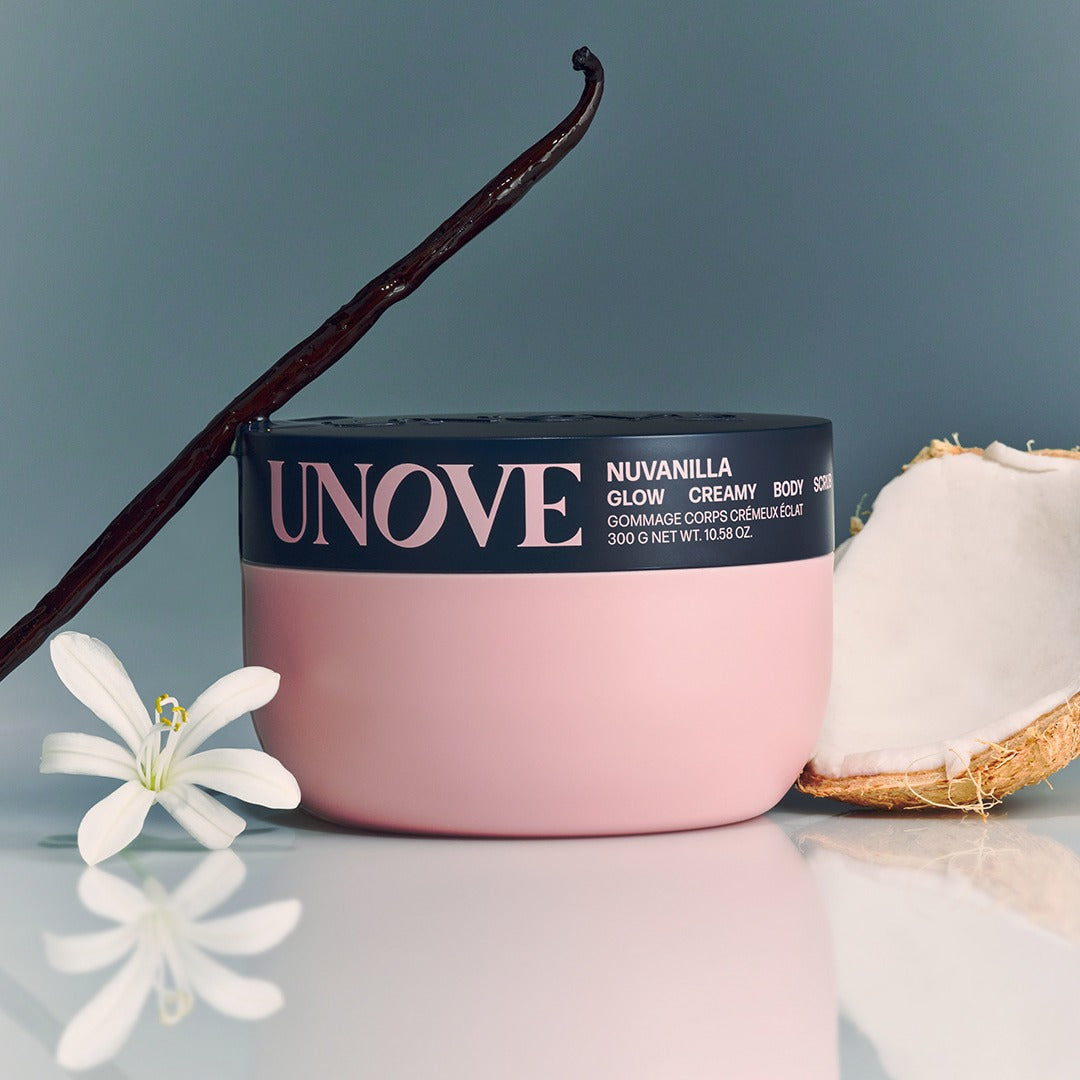 UNOVE Anove Glow Creamy Body Scrub 300g, marque UNOVE, pot rose sur fond bleu avec fleurs et noix de coco
